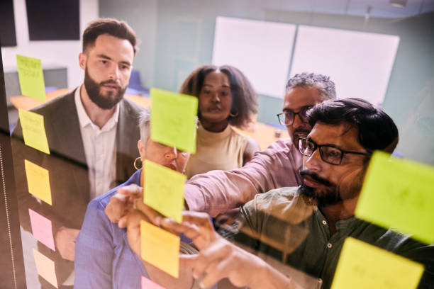 istock Diverse businesspeople brainstorming together with adhesive notes on a glass wall 1475876393