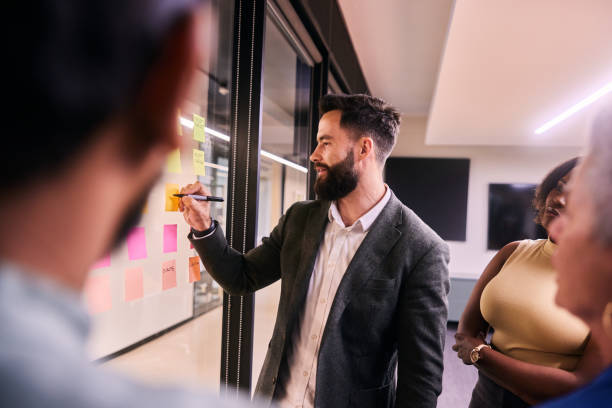 istock Businessman writing on adhesive notes during an office brainstorming session with coworkers 1475876591