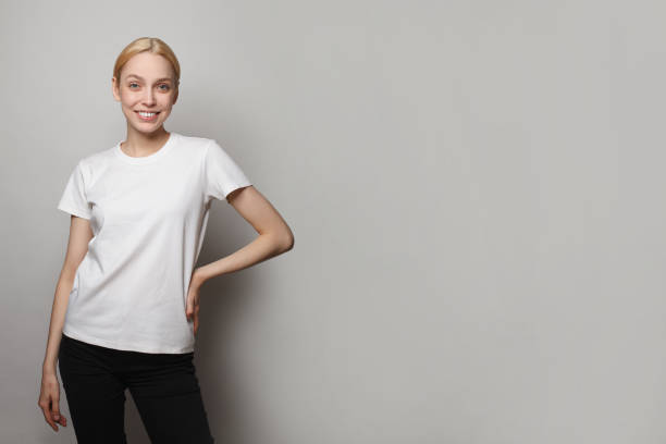 istock Young woman in white empty blank t-shirt standing against grey studio wall banner background 1475876647