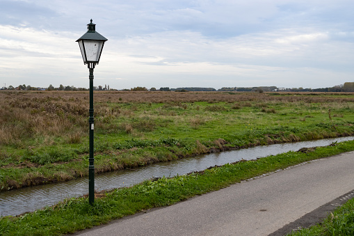 A small rural road with a light next to a beautiful green grass field in Zaanse Schans Netherlands