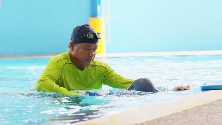 Swimming improves mood and physical strength. Senior teacher teach a boy to swim freestyle and by holding the student's arm and directing the arm in the correct direction in the pool at school. Learning and exercise during weekend.