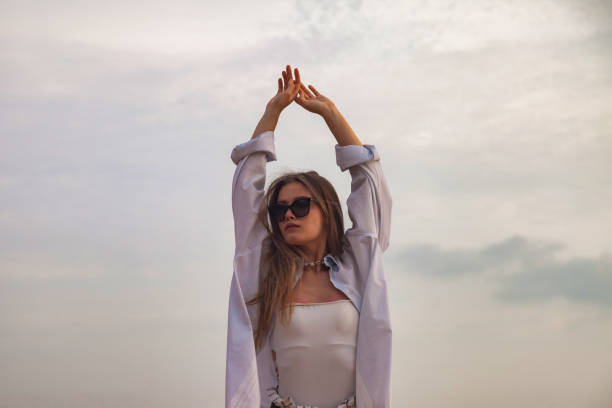 Young woman in beachwear and sunglasses posing with arms raised at blue sky background. Relaxing and enjoyable vacation on tropical sea. Travel vacation concept, summer holiday. Copy ad text space mujer joven en ropa de playa y gafas de sol posando con los brazos levantados sobre el fondo azul del cielo. vacaciones relajantes y agradables en el mar tropical. concepto de vacaciones de viaje, vacaciones de verano. copiar el espacio de texto del anunci