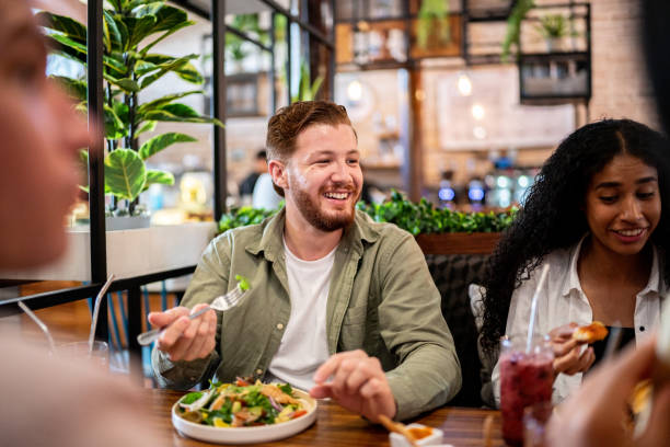joven comiendo con sus amigos en un restaurante - restaurante fotografías e imágenes de stock