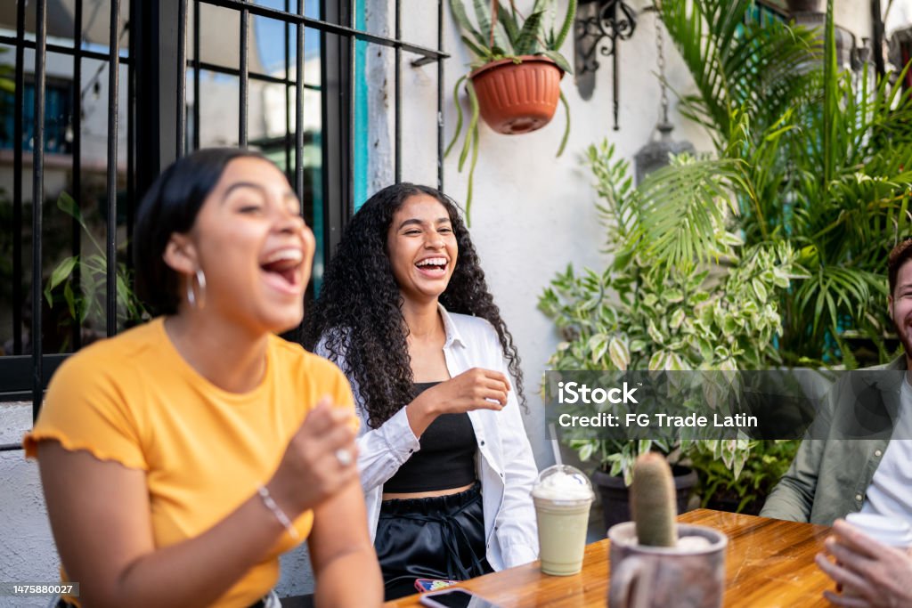 Young woman laughing while talking with her friends sitting at a table Friendship Stock Photo