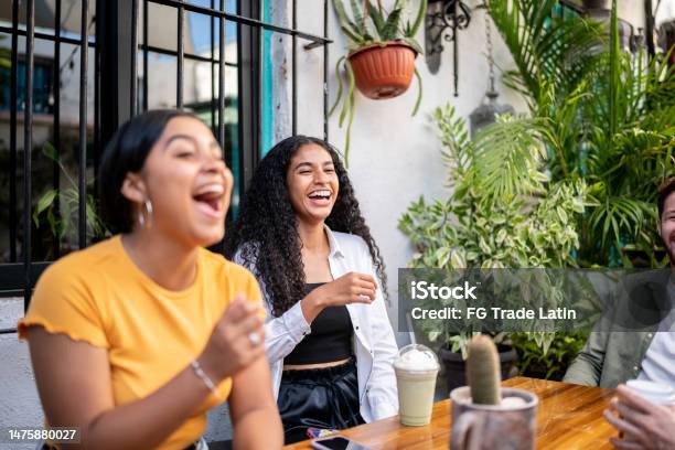 Young Woman Laughing While Talking With Her Friends Sitting At A Table Stock Photo - Download Image Now