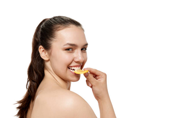 istock Cheerful adorable young with bared shoulders tasting orange fruit over white background. Closeup. Beauty, fashion, skincare, emotions, ad 1475883857