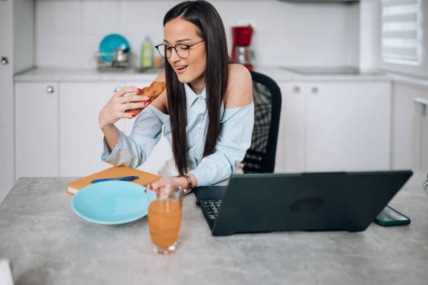 istock Young woman enjoying a croissant while working on laptop 1475885171