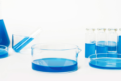 Bowl for the laboratory with a blue, blue liquid. Against the background of laboratory glassware. Petri dishes, flasks, test tubes. On a white, light background.