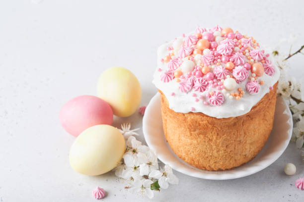 istock Traditional Easter sweet bread or cakes with white icing and sugar decor, colored eggs and cherry blossom tree branch over white table. Various Spring Easter cakes. Happy Easter day. Selective focus. 1475886309