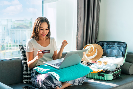 Happy Asian woman using credit card booking flight tickets and hotel at home. Planning a trip and online booking, cashless society, technology and lifestyle, Summer vacation concept. Free space