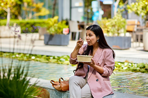 Three-quarter front view of corporate professional sitting outdoors in springtime sunshine and enjoying midday meal.