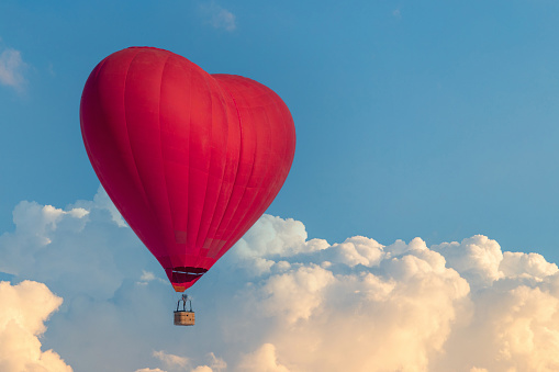 A hot air balloon in the shape of a red heart flies above the clouds. Unusual date surprise lovers.