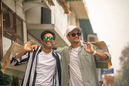 Two handsome men laughing and spending leisure time together after shopping in city