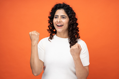 Portrait of beautiful cheerful young woman make hold fists looking at camera on orange background
