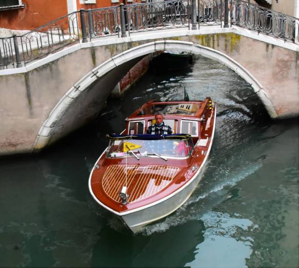 Venice - Water Taxi Venice, Italy - October 12, 2021. The image shows a water taxi in the back street canals in the San Polo district. Water taxis in Venice are common place, but they are also very expensive. They are typically well maintained boats, some made out of word and have some element of grandeur. watertaxi stock pictures, royalty-free photos & images