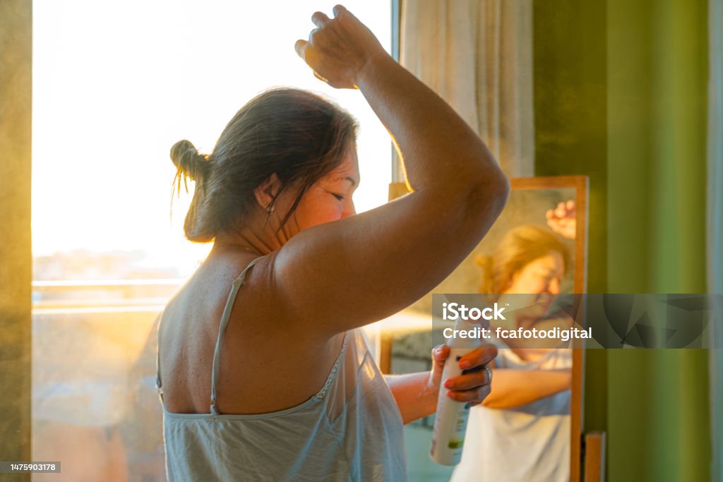 Woman applying deodorant on underarm Portrait of  mature woman applying deodorant on underarm in front of a mirror during morning time. High resolution 42Mp indoors digital capture taken with SONY A7rII and Zeiss Batis 40mm F2.0 CF lens Deodorant Stock Photo