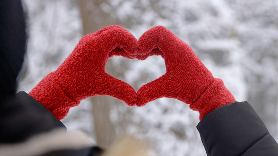 An unrecognizable woman has her hands in the shape of a heart, an expression of excitement, joy, love and happiness. The photo was taken on a hiking trail in a beautiful snowy forest.