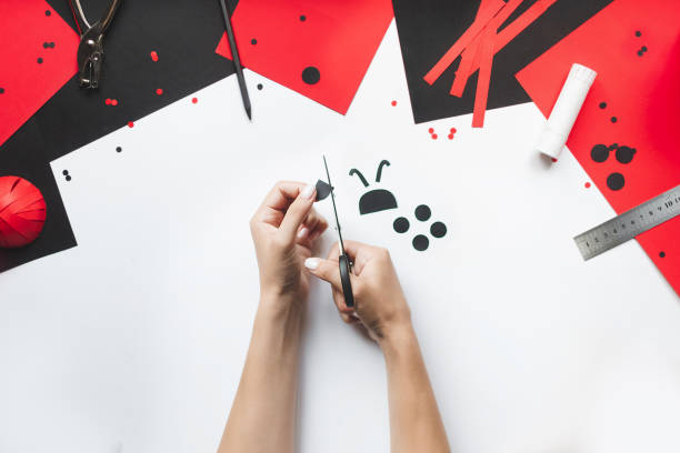 istock How to make paper red and black ladybug toy with children at home. Step by step instructions. Hands making DIY summer project. Top view. Step 10. Сut out dots and the ladybugs face 1475910893