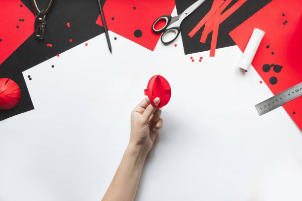 How to make paper red and black ladybug toy with children at home. Step by step instructions. Hands making DIY summer project. Top view. Step 8. Glue the next strip crosswise