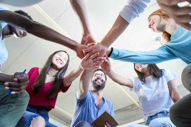 Low angle view of a group of happy young students with teacher stacking hands hands . stock photo