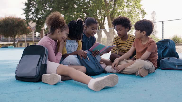 School, playground and friends reading story books together while sitting outdoor during their break. Education, book or learning with girl and boy students outside class bonding during recess