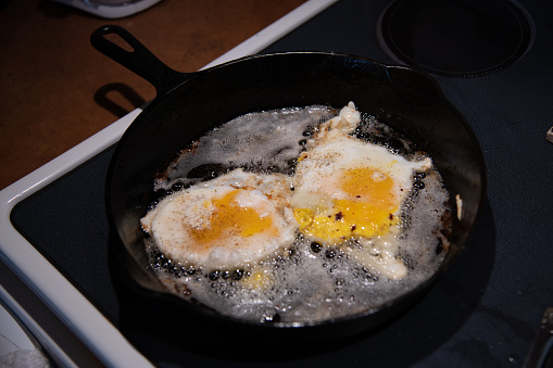 Frying fresh farm raised chicken eggs in iron skillet in western USA of North America.