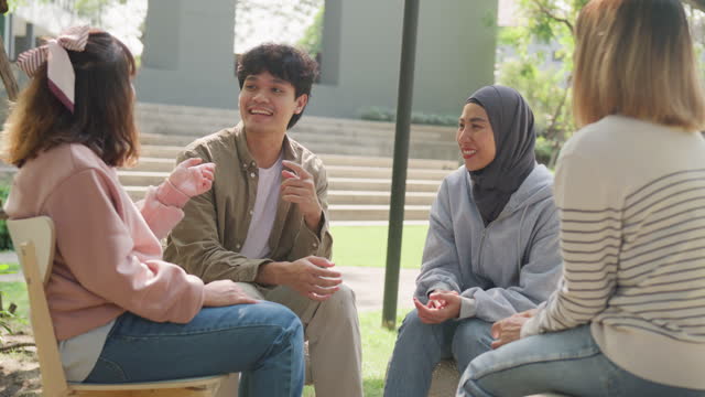 Small Asian group of people sit in a close circle and talk to a therapist in park. Smile people sharing story happy speak diverse people sitting in circle at group therapy session psychologist.
