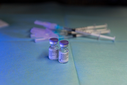 two vials of vaccine with syringes in the background