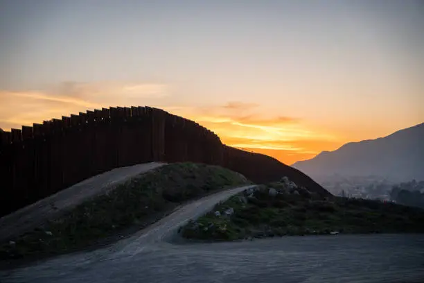 Photo of International Border Wall Between Tecate California and Tecate Mexico Near Tijuana Baja California Norte at Dusk Under Stunning Sunset with View of the City From the USA