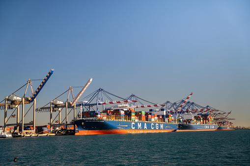 Aerial view of a fully loaded container LNG-powered ship pulled by tugboats for departure