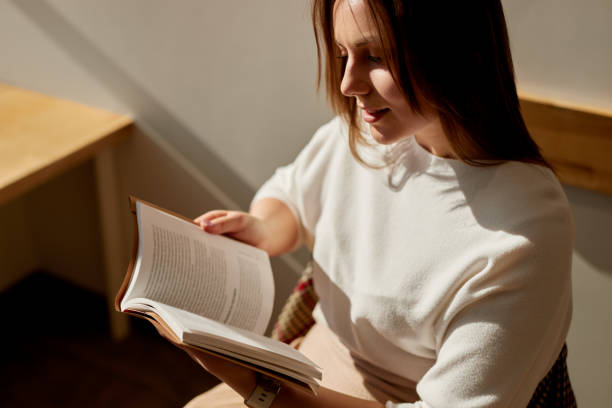 istock Young woman reading book at home 1475933377