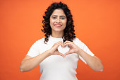 Photo of happy girl making demonstrating heart on chest on orange background, stock photo