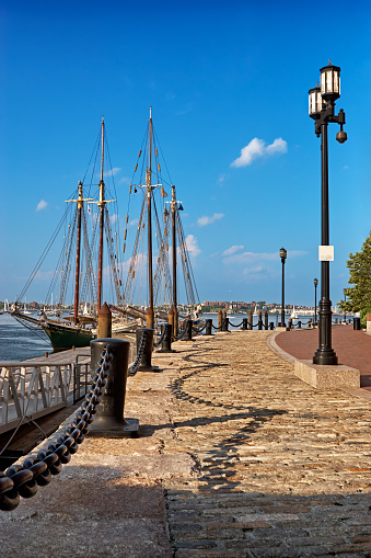 A sunny summer day on Boston's cobblestone harborwalk with tall ships tied up in the harbor