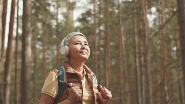Mature Asian Woman in Headphones in Forest