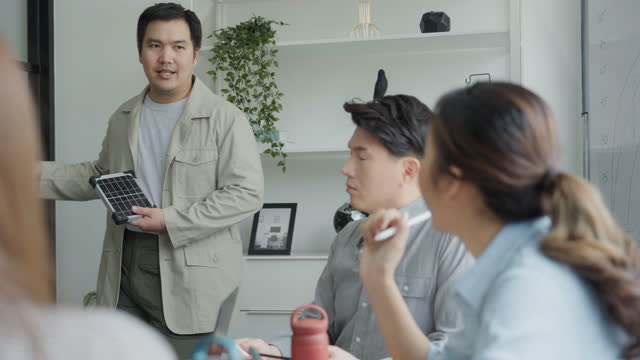 Young asian male entrepreneur presenting his small solar panel to his coworkers on a business meeting.