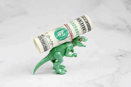 Small green dinosaur carries roll dollar on his back, rope strangles his neck, with copy space