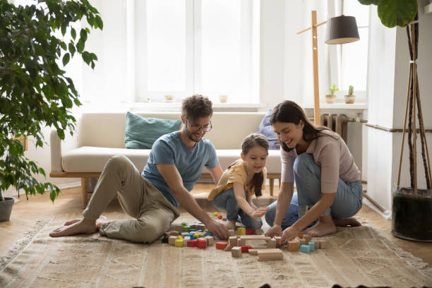 Positive young parents and cute kid playing with toy blocks stock photo