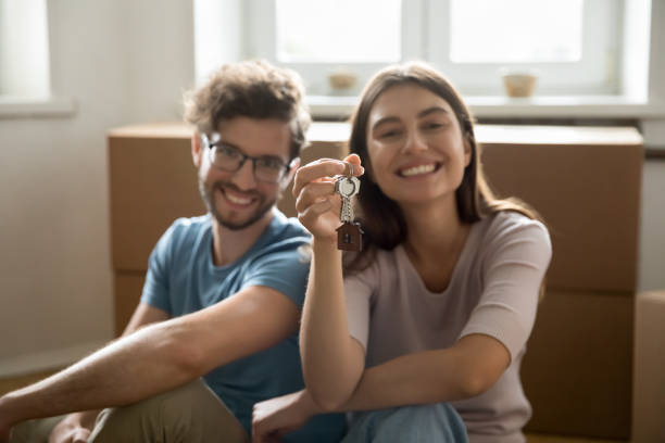 Happy young couple showing keys from hew home together Happy young couple showing keys from hew home together, looking at camera, smiling, sitting at cardboard relocation boxes, feeling happy, enjoying moving into new flat, apartment, house happy family with key of their new house stock pictures, royalty-free photos & images