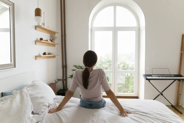 Back view of relaxed young woman sitting on bed