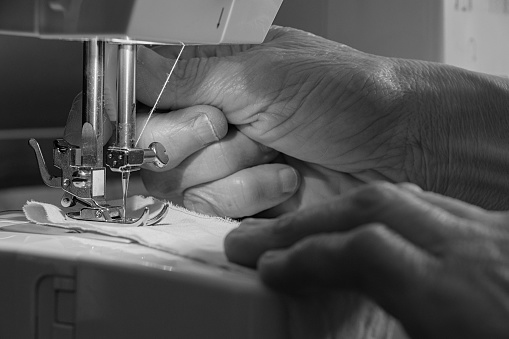 Happy seamstress sewing clothes at an atelier using a machine - small business concepts