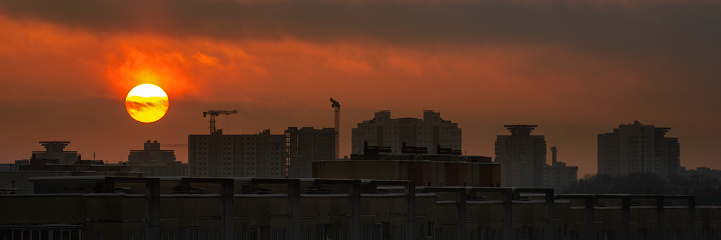 a dramatic red sunset over a city block with a sun disk above the rooftops. widescreen panoramic side view