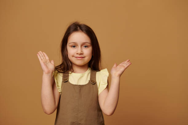criança da idade elementar, uma menina adorável, sorrindo bonito para a câmera, segurando as palmas das mãos para cima no fundo bege isolado - palm up - fotografias e filmes do acervo