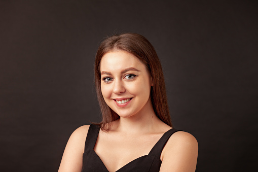 Close-up studio portrait of a cheerful young white woman with long brown hair against a black background