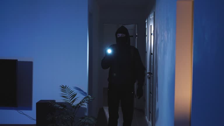 An unrecognizable masked burglar has broken into the apartment and is looking for valuables to steal. A man in dark clothes and with a flashlight in his hands.