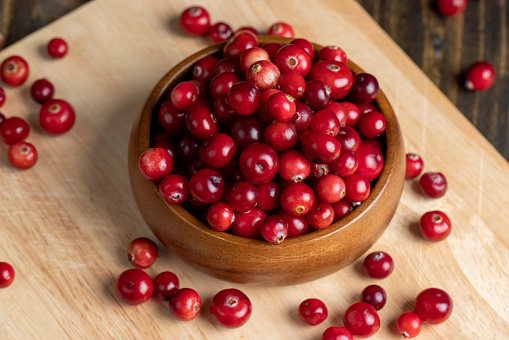 A small white bowl full fresh cranberries on a white textured surface.