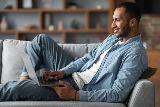 istock Smiling African American Man Using Laptop While Relaxing On Couch At Home 1476000664