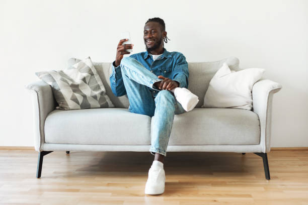 istock African American Guy Using Smartphone Sitting On Couch At Home 1476000684
