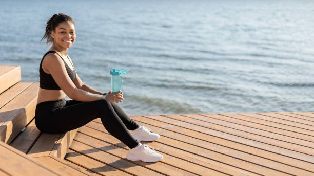istock Happy black woman jogging by seaside, drinking water 1476001663