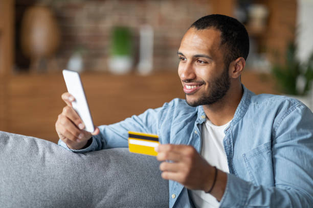 istock Mobile Payments Concept. Smiling Black Guy Using Smartphone And Credit Card 1476001729