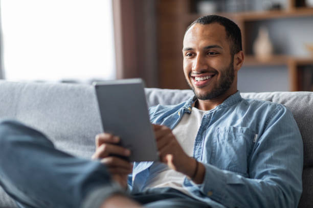 istock Handsome smiling black male relaxing with digital tablet at home 1476001835